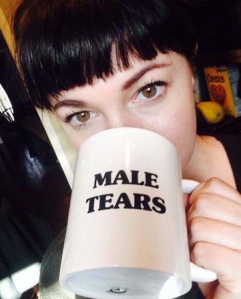 An attractive lady struggles to remove a 'male tears' mug from her face. Superglued rims are no joke :'(